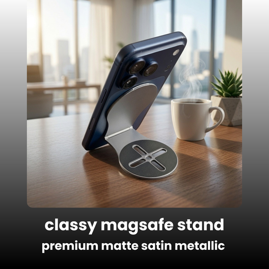 A magnetic magsafe phone stand made of premium matte satin metallic, shown holding a dark blue smartphone on a wooden table in a bright, modern office setting. A white coffee mug and a small potted plant are visible in the background.