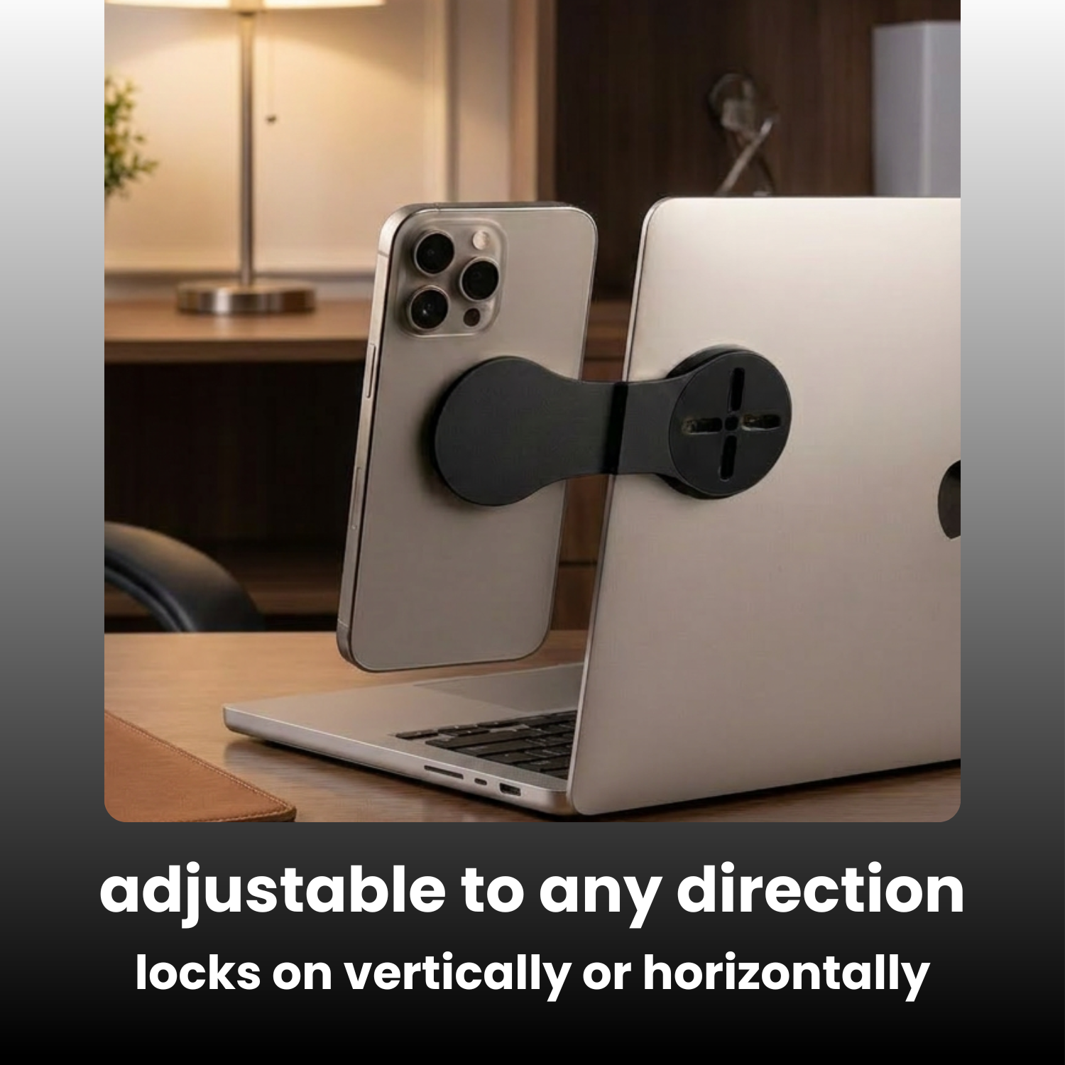 A black magnetic phone stand adapter shown between a silver smartphone and a silver laptop on a desk, with text at the bottom reading 'adjustable to any direction locks on vertically or horizontally'.