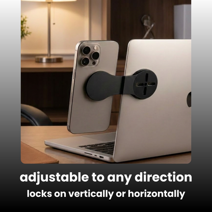 A black magnetic phone stand adapter shown between a silver smartphone and a silver laptop on a desk, with text at the bottom reading 'adjustable to any direction locks on vertically or horizontally'.